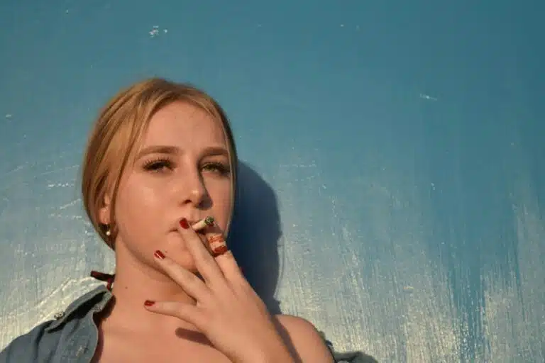 a woman smoking a cigarette in front of a blue wall