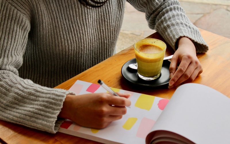 person holding pen with coffee on table