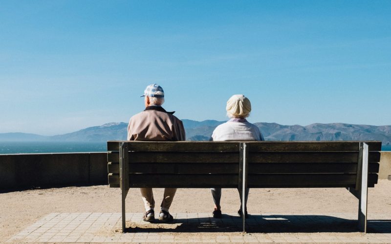 man and woman sitting on bench facing sea