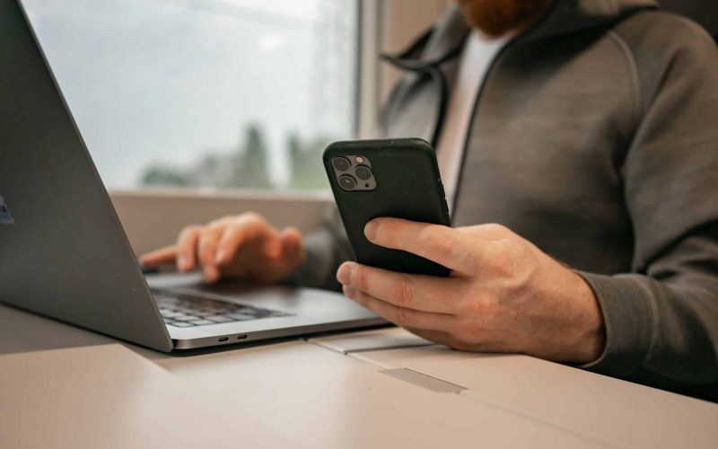 a man sitting in front of a laptop computer holding a cell phone