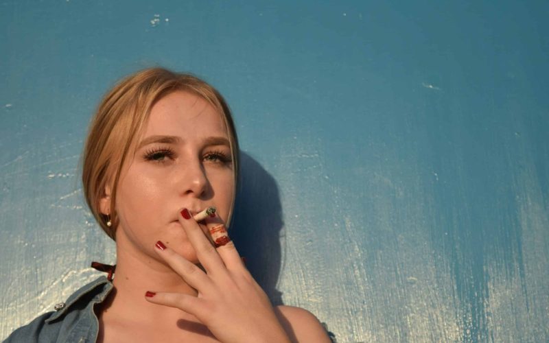 a woman smoking a cigarette in front of a blue wall